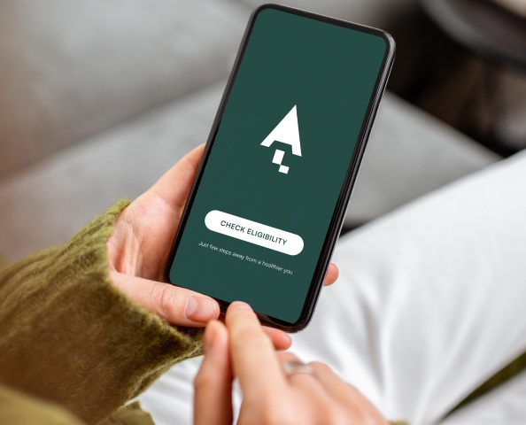 Person holding a smartphone with a green screen displaying a white arrow symbol and a "Check Eligibility" button.