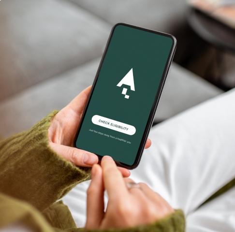 Person holding a smartphone displaying a green screen with a logo and "Check Eligibility" button.