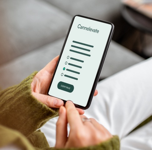 A person holds a smartphone displaying a survey with multiple-choice options and a "Continue" button. The screen shows the word "Cannelevate.