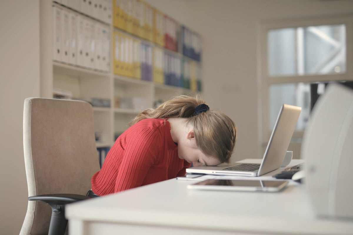Tired woman resting her head on her desk beside her laptop