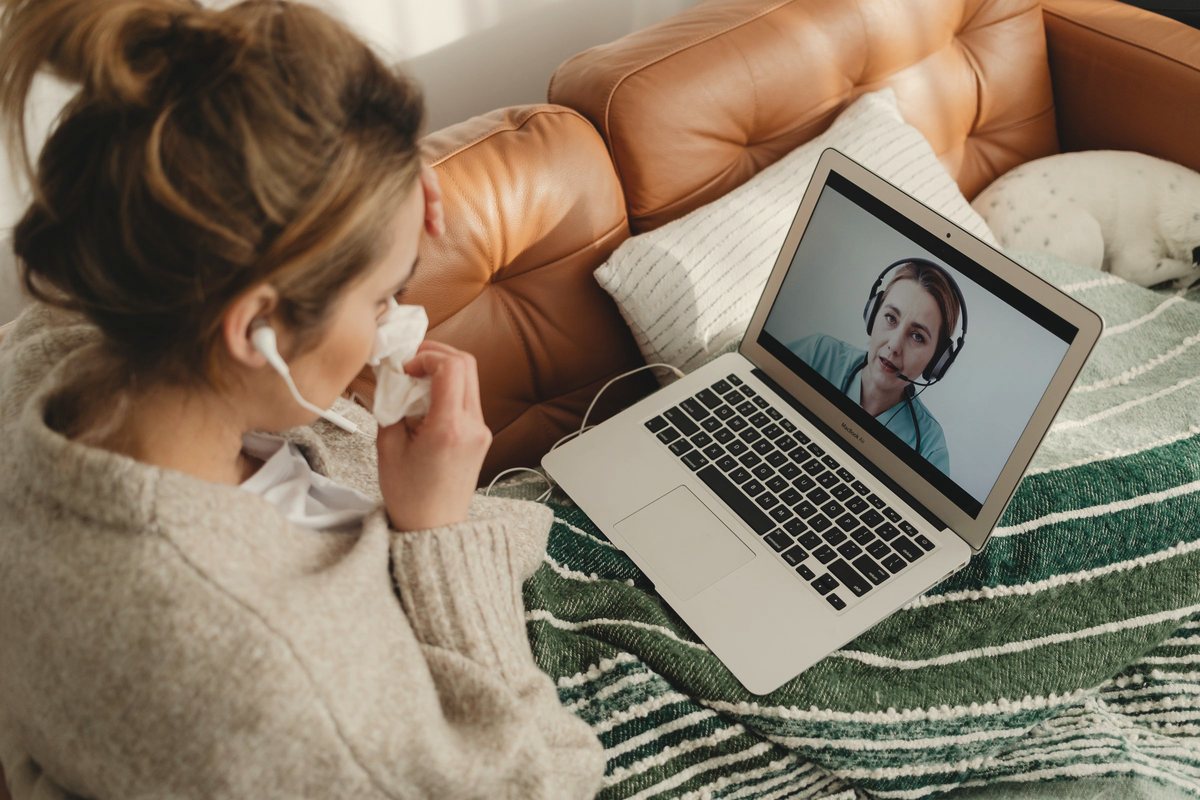 Woman with earphones on a video call, her laptop resting on a cushion beside her on the couch