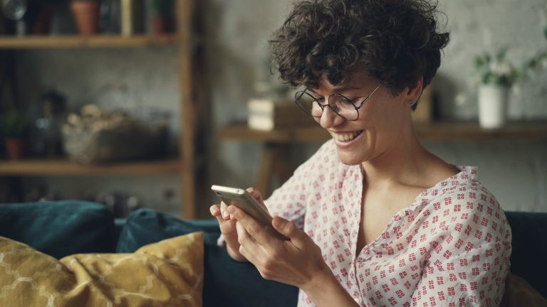 Smiling woman using her smartphone on a sofa at home