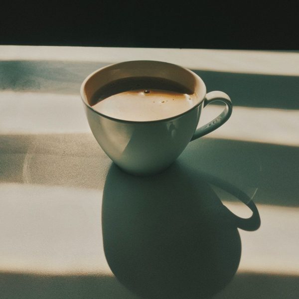 White coffee cup on a table in warm morning sunlight with soft shadows