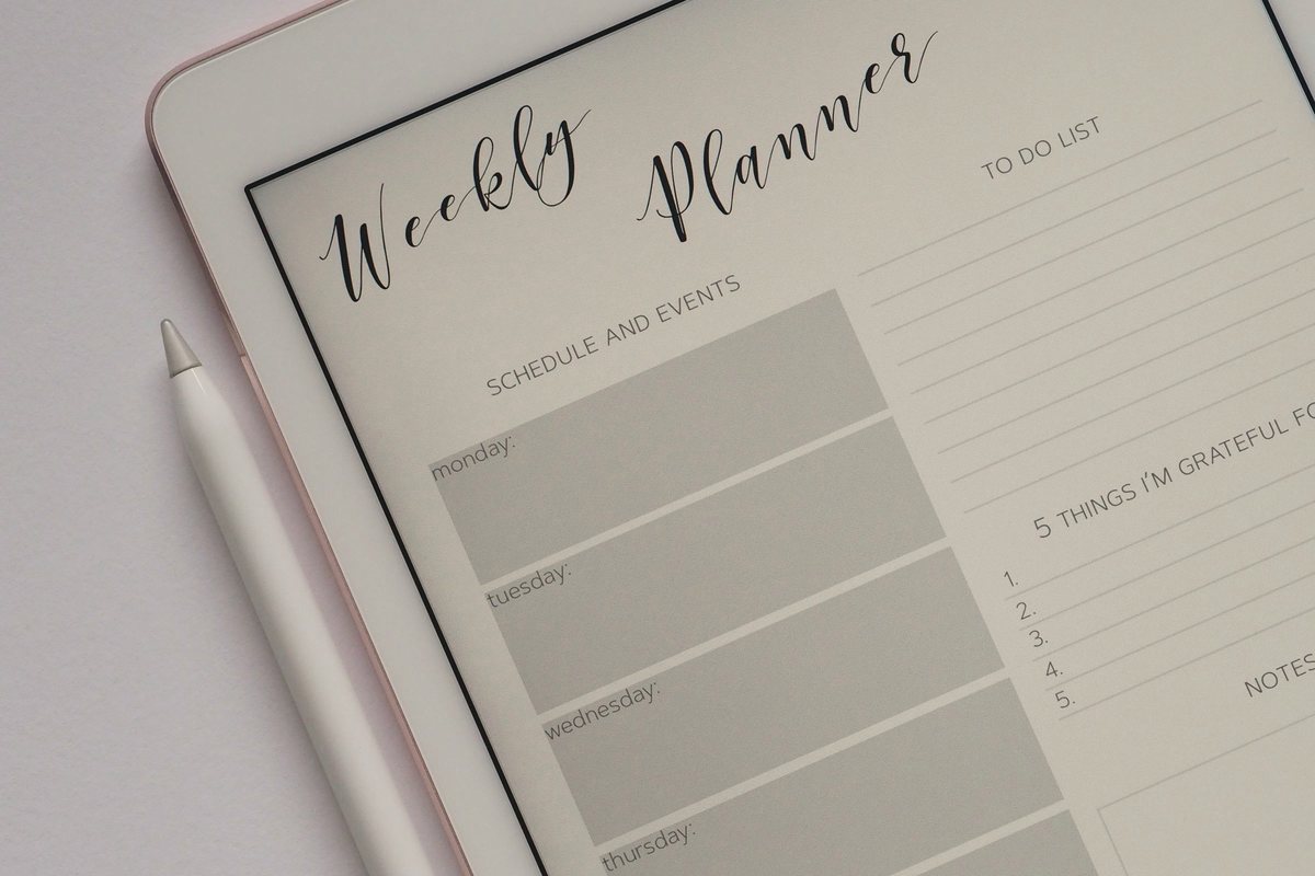 Tablet showing a weekly planner template beside a stylus on a light desk