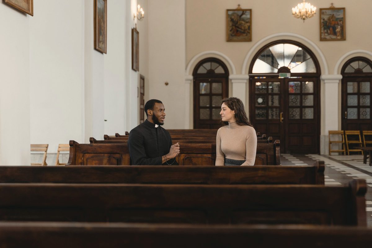 Priest and woman sitting on church pew having a conversation