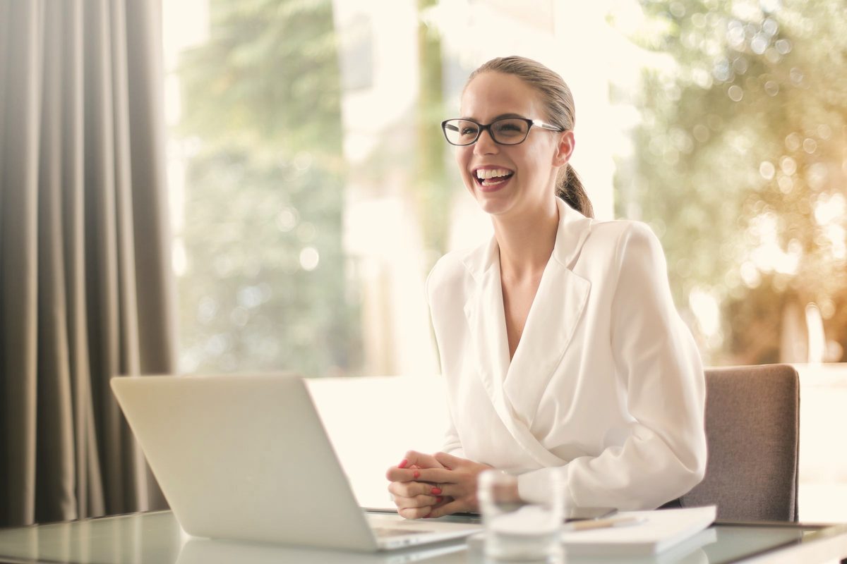 Woman laughing while working on her laptop in a bright office