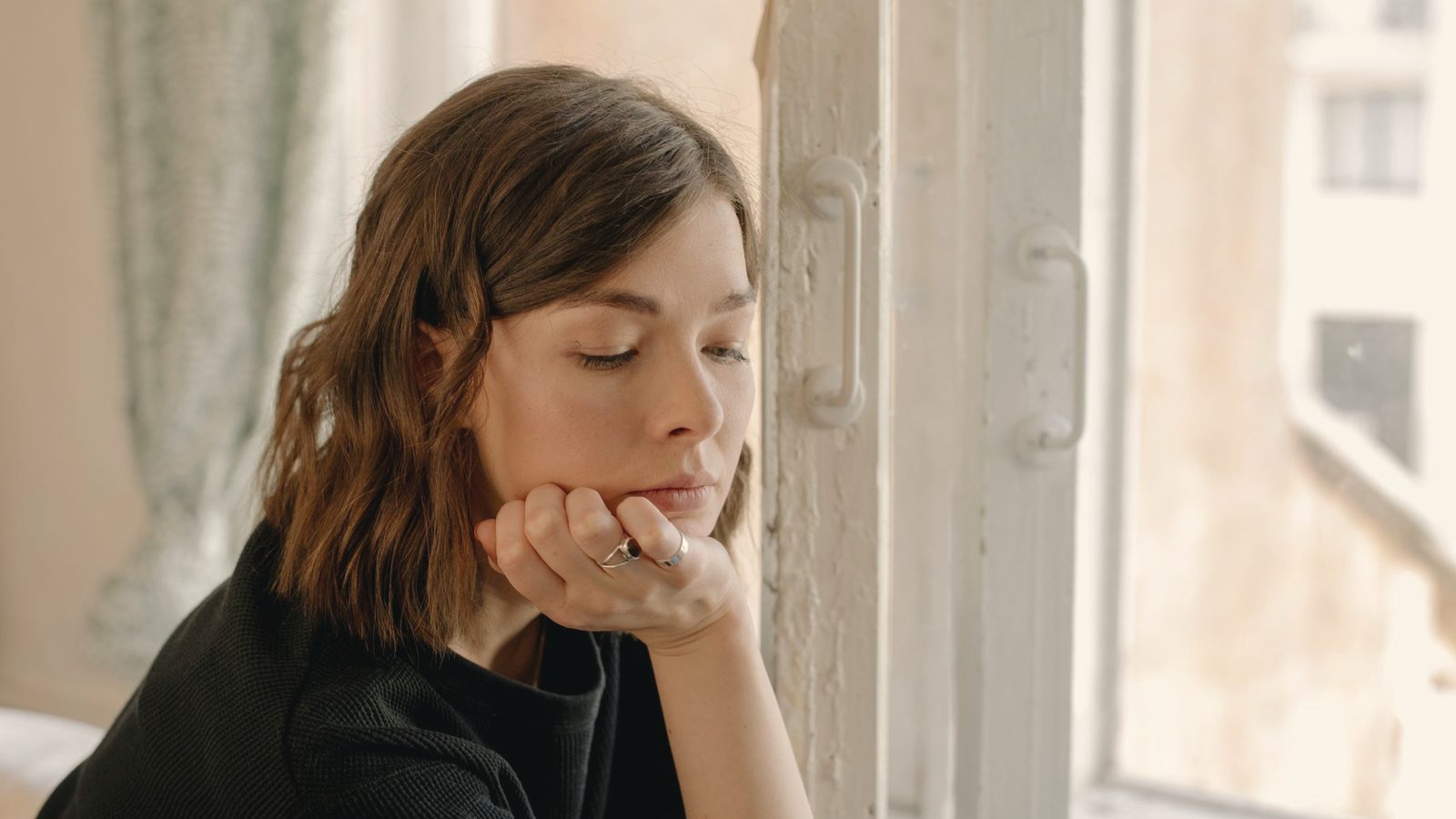 Woman in shirt leaning on white wooden window