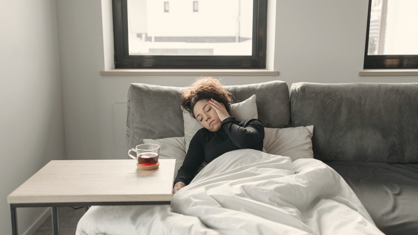 Woman resting on a couch under a white duvet with a cup of tea nearby