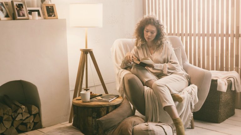 Woman reading a book in a lamp-lit armchair during her evening wind down routine