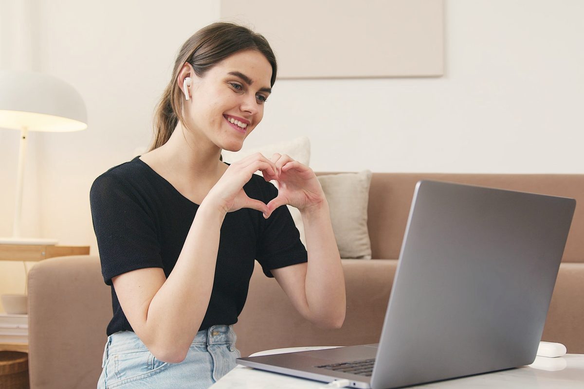 Smiling woman making a heart shape with her hands during a video call