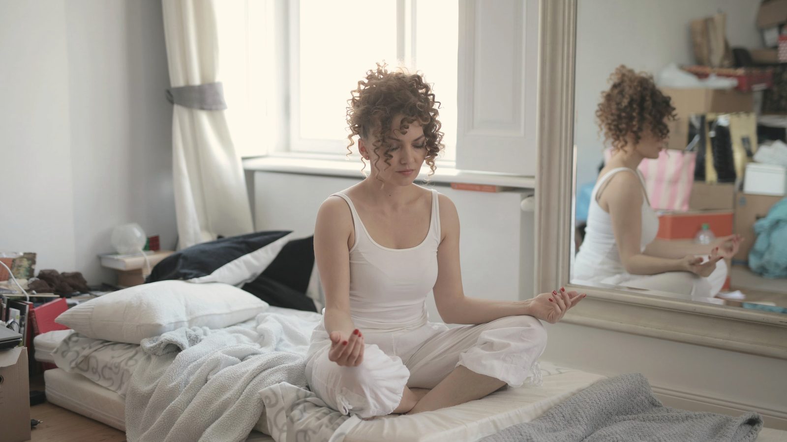 Woman sitting cross-legged on her bed meditating in the morning