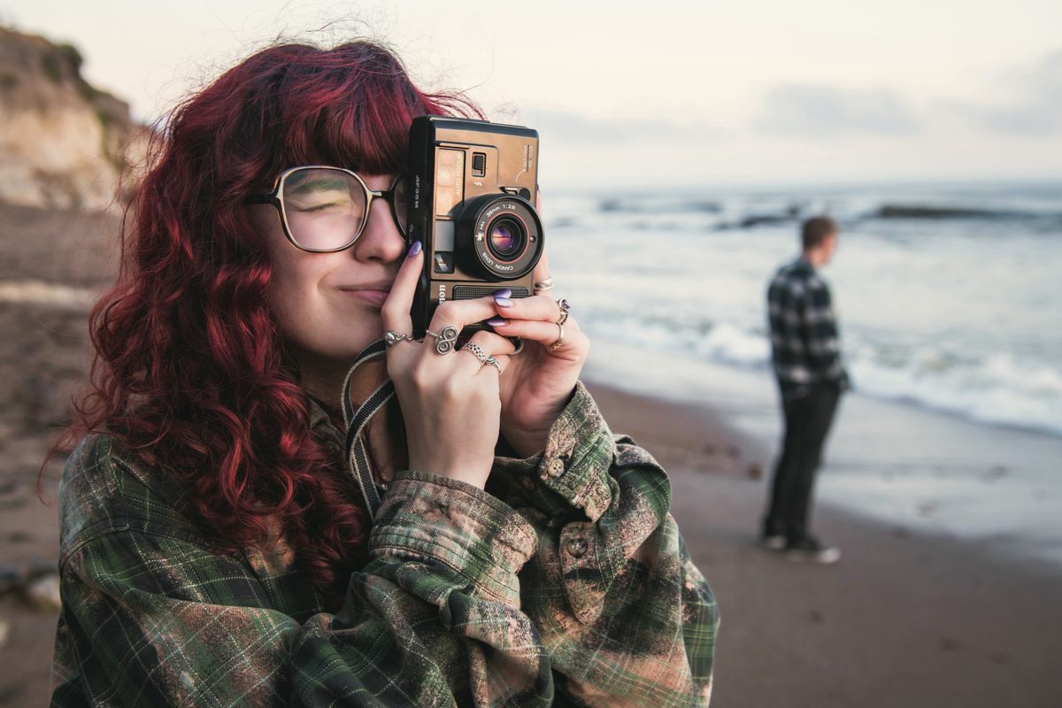 Young woman taking a picture with a film camera on the beach