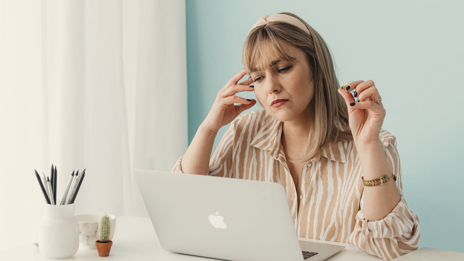 Woman at a laptop holding her head, feeling stressed while working from home