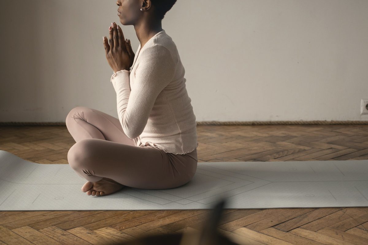 Woman sitting cross legged with her hands clasped and eyes closed on a yoga mat