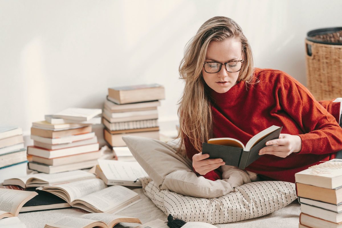 Focused woman reading book near various literature