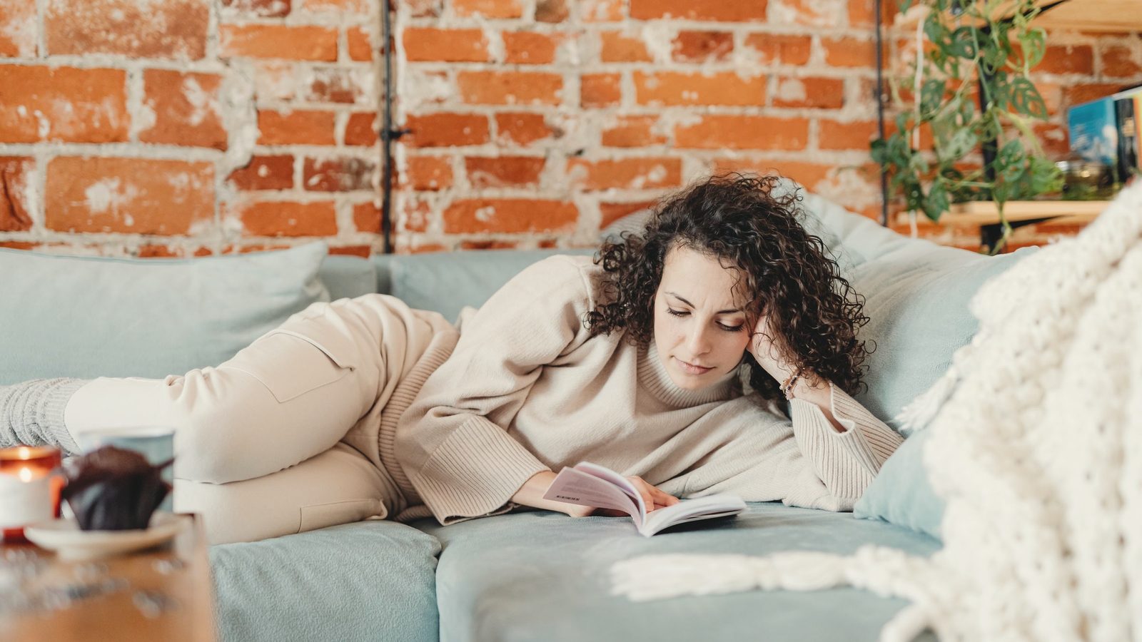 Woman lying on a couch while reading a book