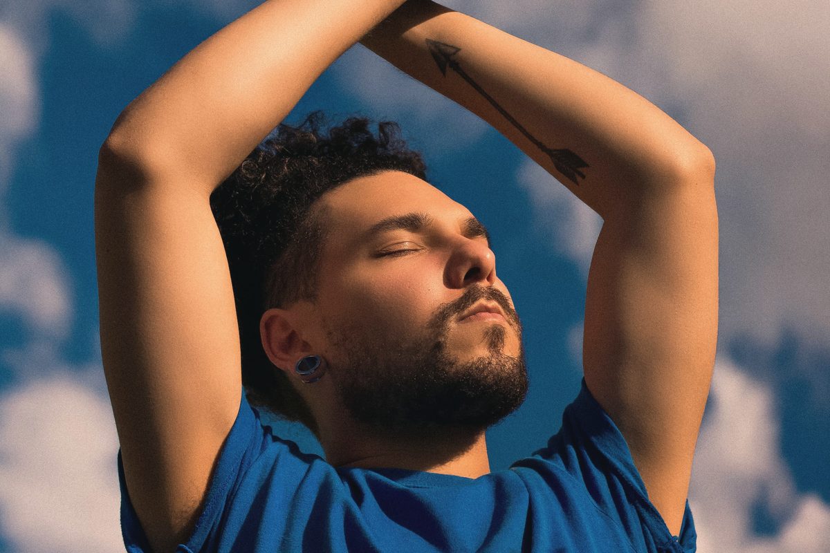 Man with raised arms and closed eyes under an open sky