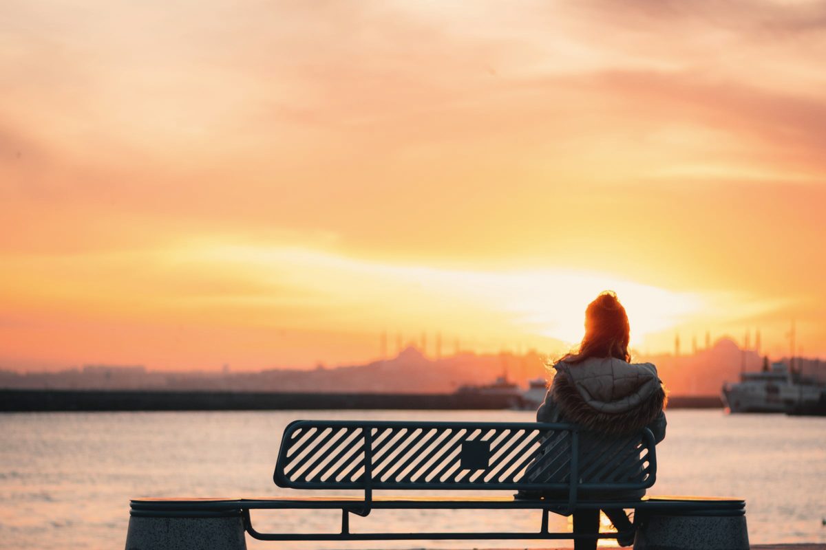 Woman sitting on a metal bench while looking at the golden sky
