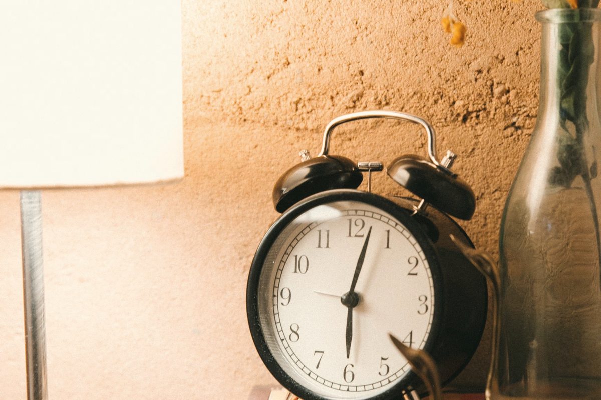 Vintage alarm clock and luminous lamp placed on bedside table
