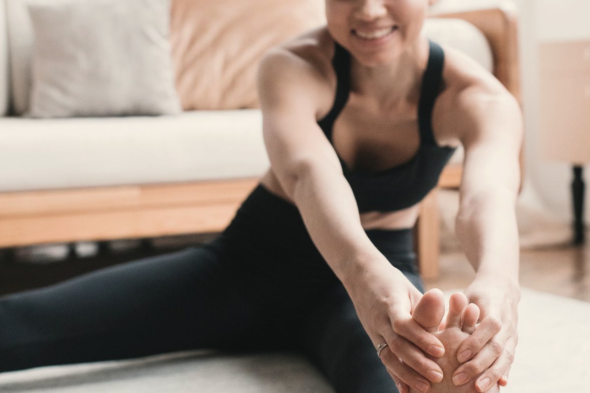 Woman doing a seated hamstring stretch on an exercise mat at home