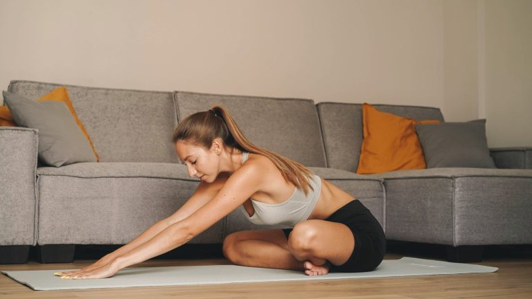Woman doing a seated forward stretch on an exercise mat in her living room