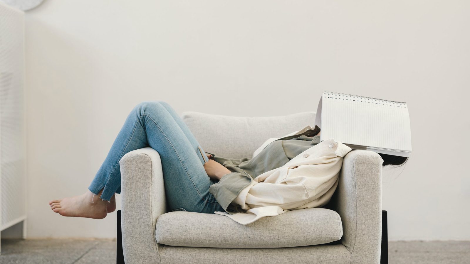 Person resting in an armchair with a notebook over their face