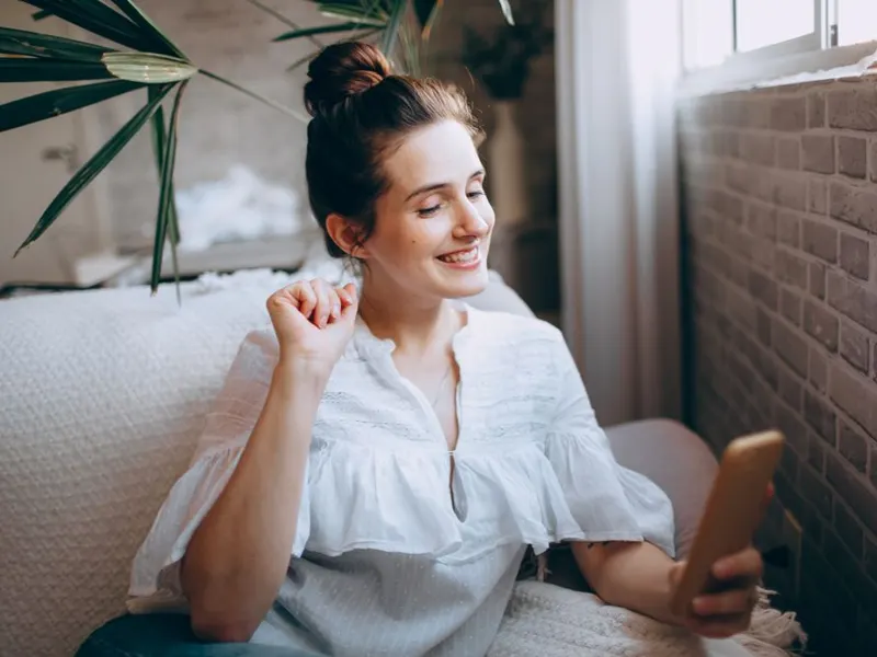 Smiling woman checking her phone on the sofa at home