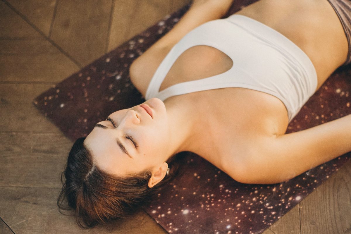 Woman lying on a mat relaxing beside candles