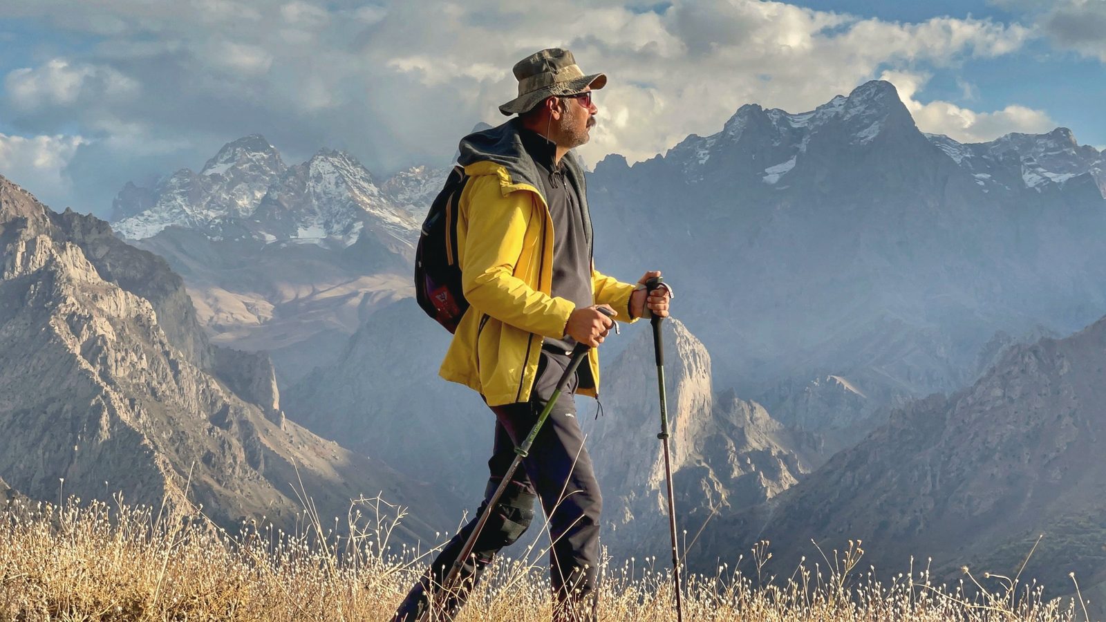 Man in hat and yellow jacket hiking in mountains