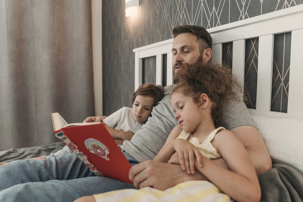 Father reading a book to his children in bed