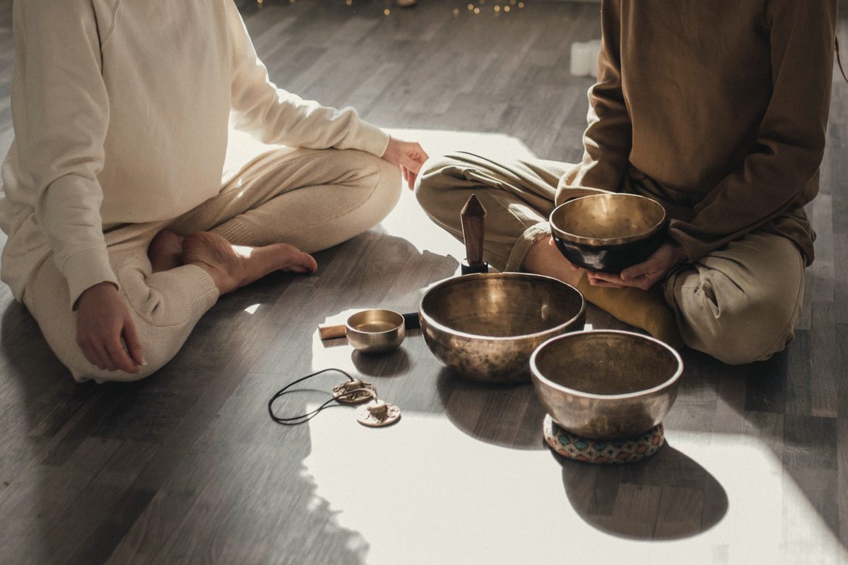 Two people sitting on the floor with brass singing bowls