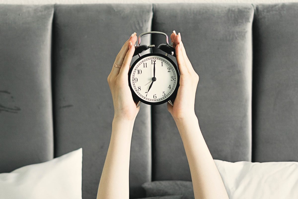 Hand holding up an alarm clock in bed