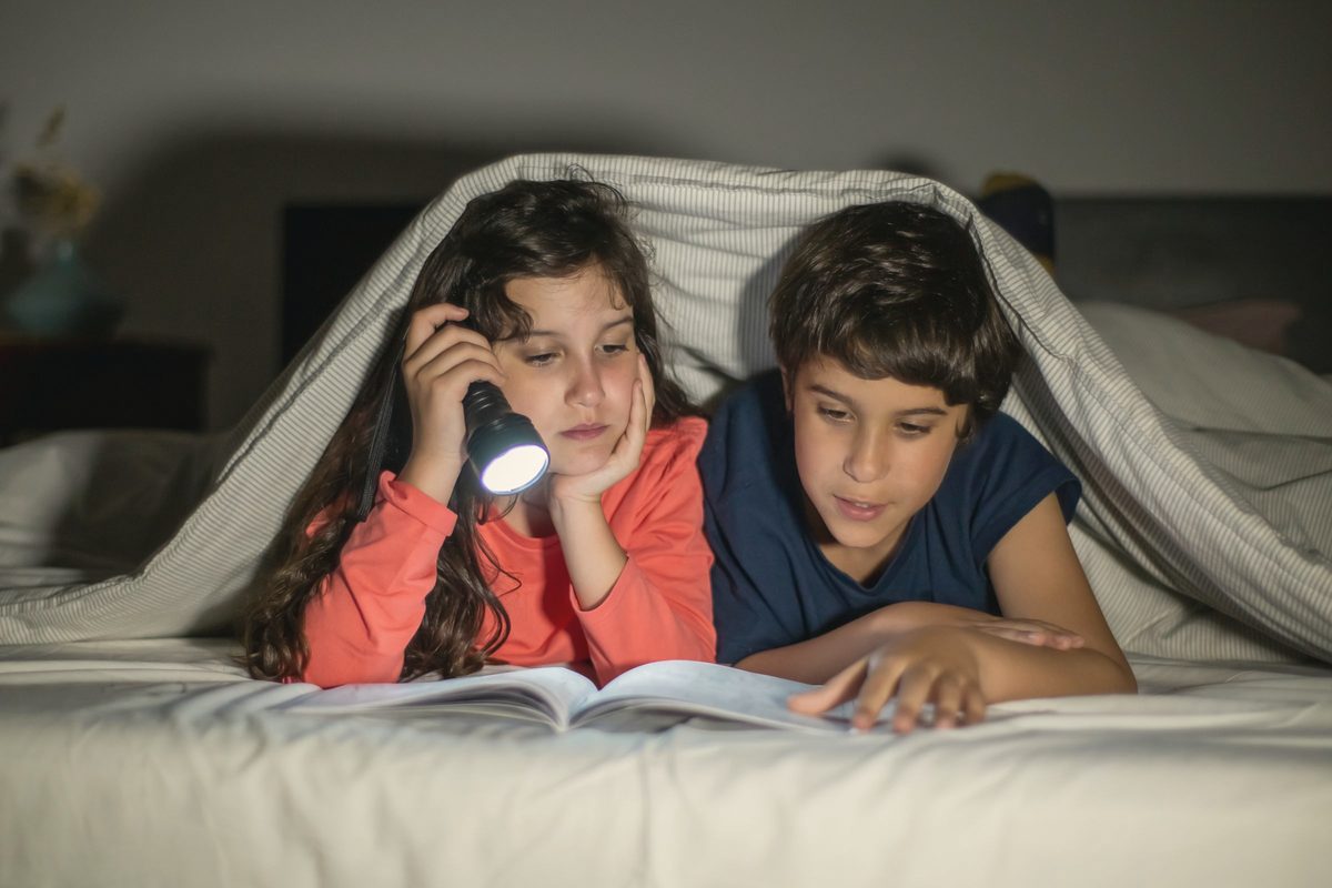 A girl and a boy under a blanket reading a book