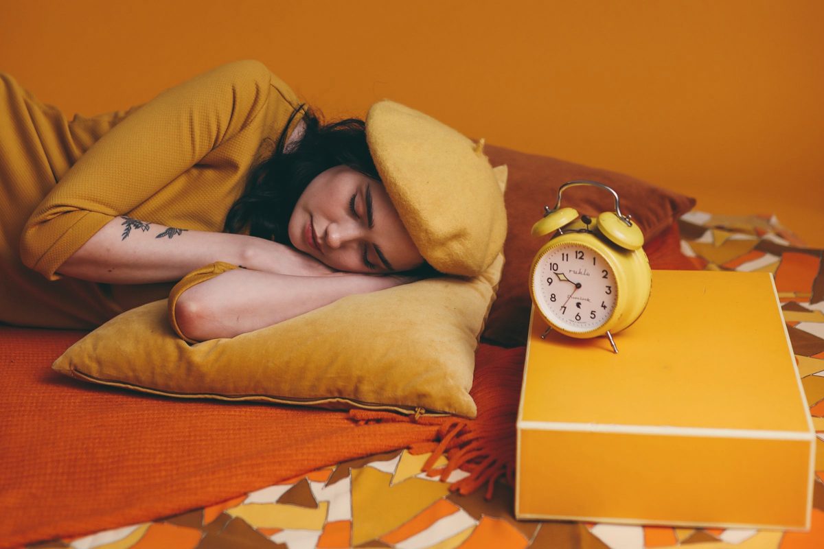 Woman lying on bed beside a yellow analog alarm clock