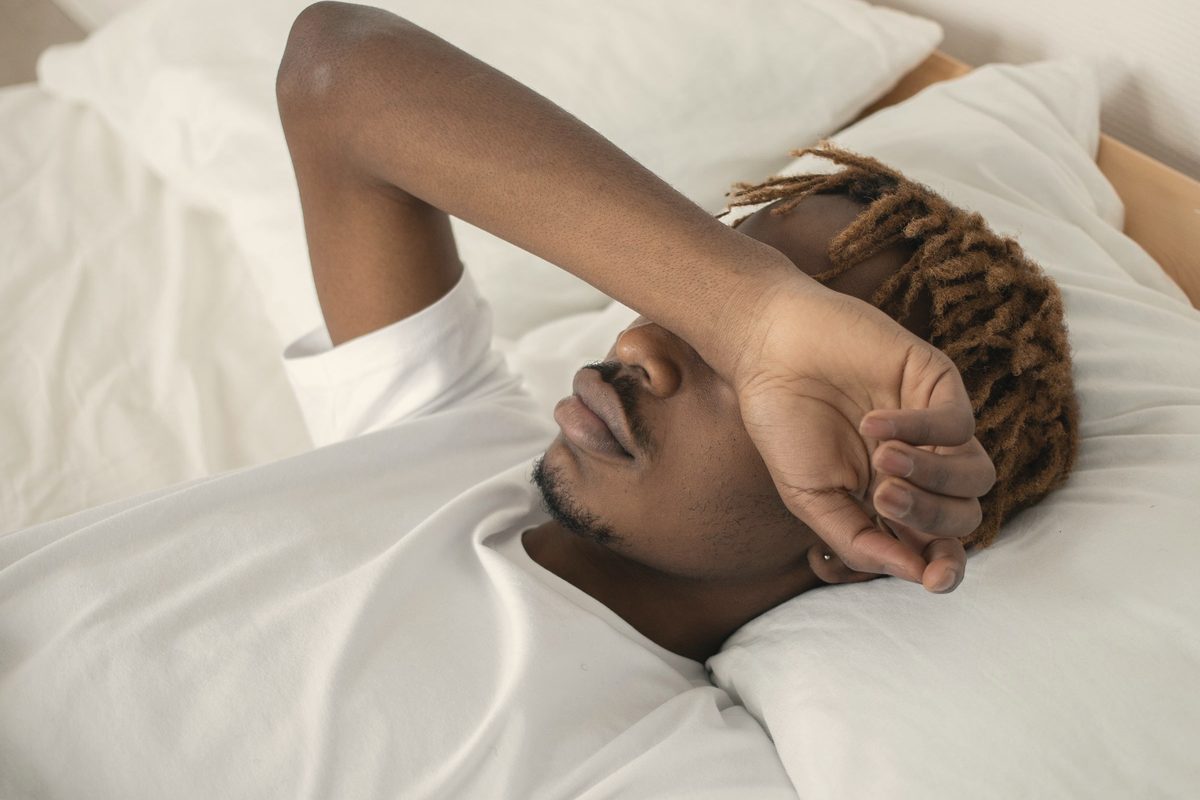 Man lying in bed resting his arm across his eyes
