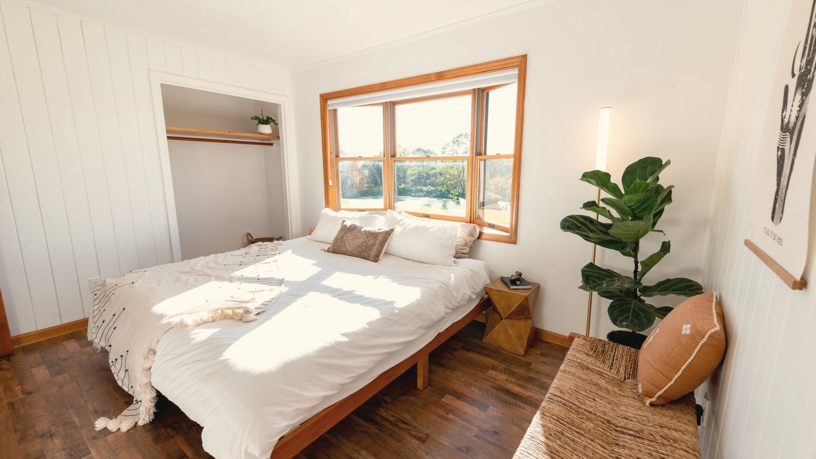 Bright bedroom with white linen, timber floor and a window letting in daylight