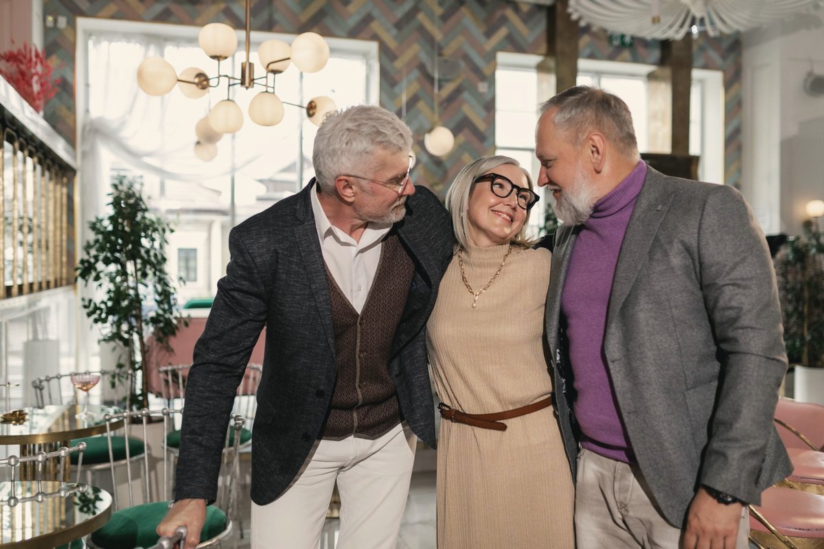 Three older friends laughing and hugging in a bright cafe