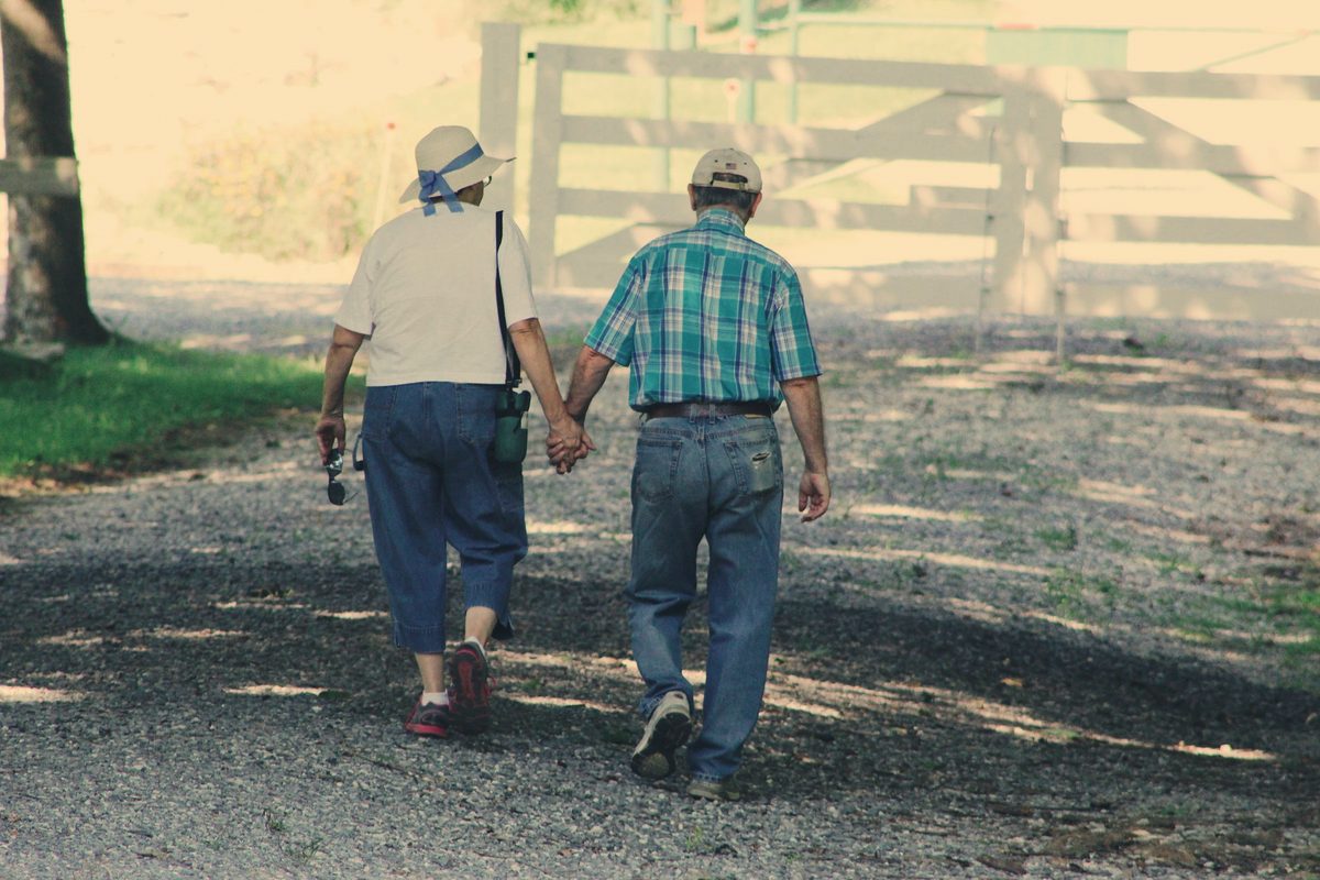 Older couple walking hand in hand along a country path
