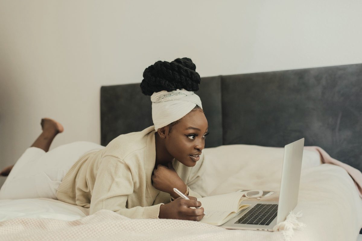 Woman taking notes while reading on a laptop