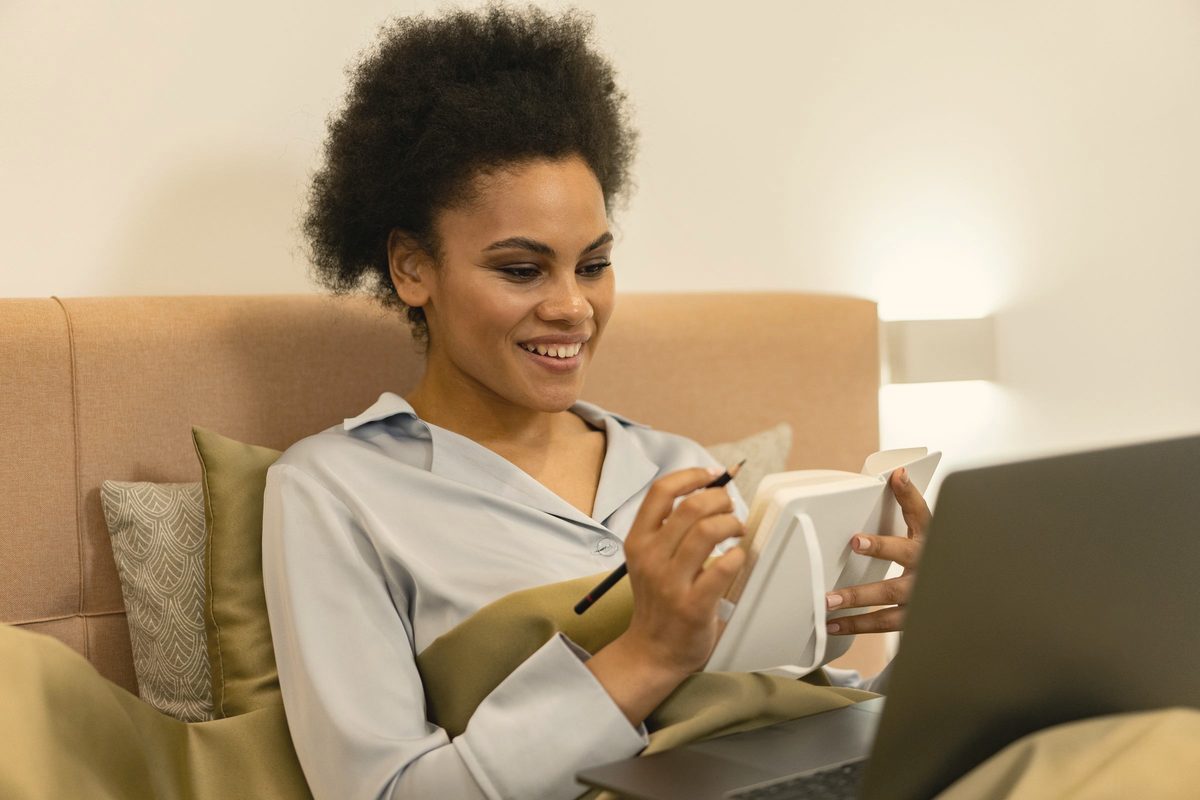 Woman reading her laptop screen with a notebook and pencil