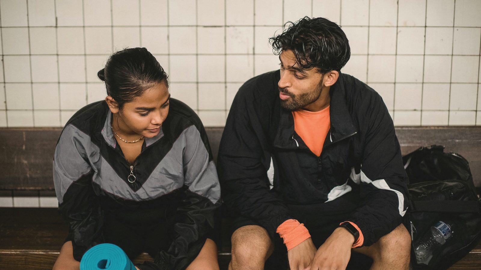 Two young sport people resting after fitness exercises in changing room