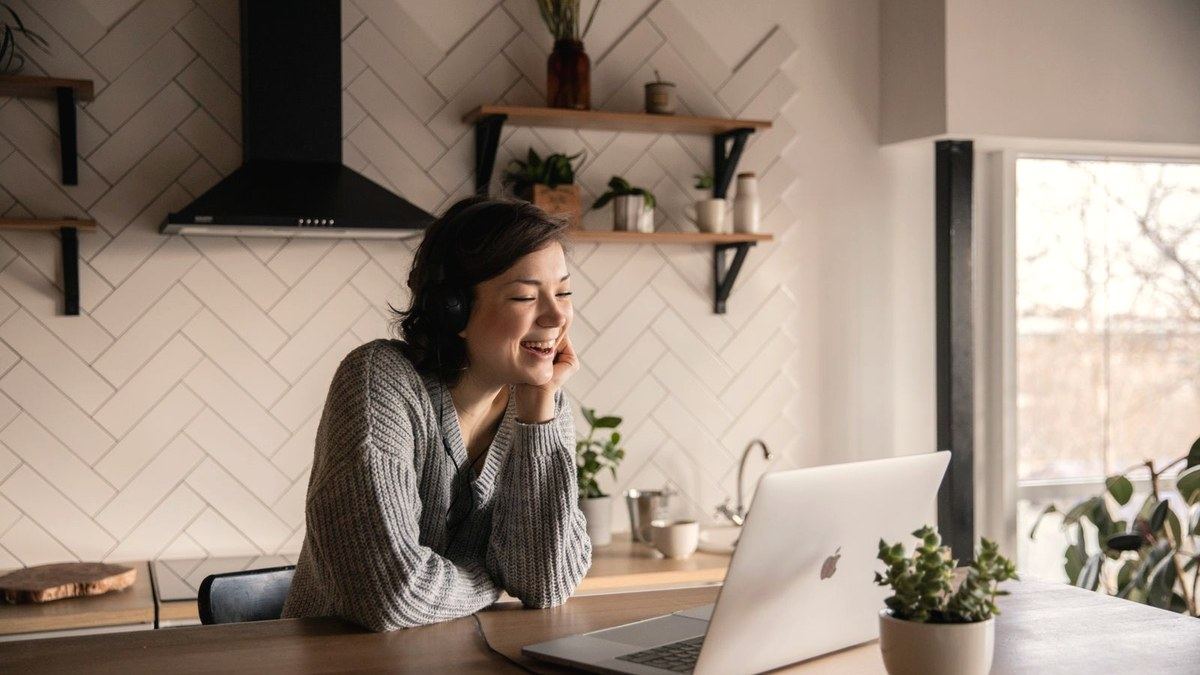 Woman smiling on a telehealth consult at her laptop in a bright kitchen