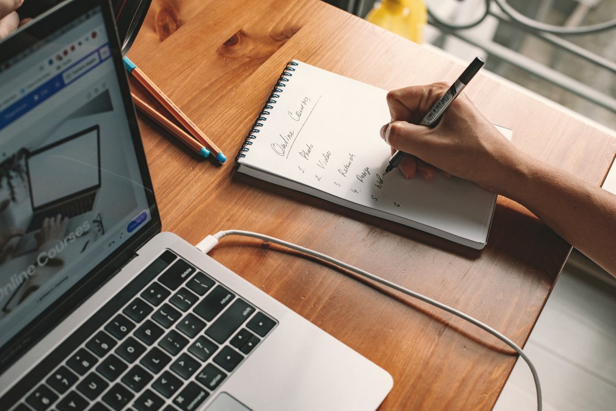 Hand writing a numbered list in a notebook next to an open laptop