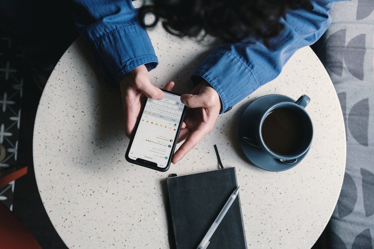 Person typing on a phone at a table with a notebook and coffee cup