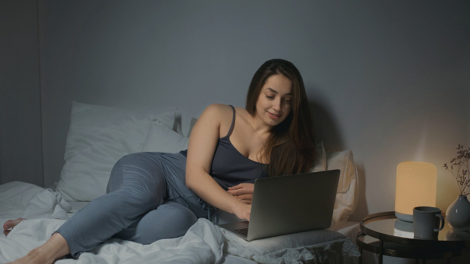 Woman relaxing in bed with a laptop under warm evening lamp light
