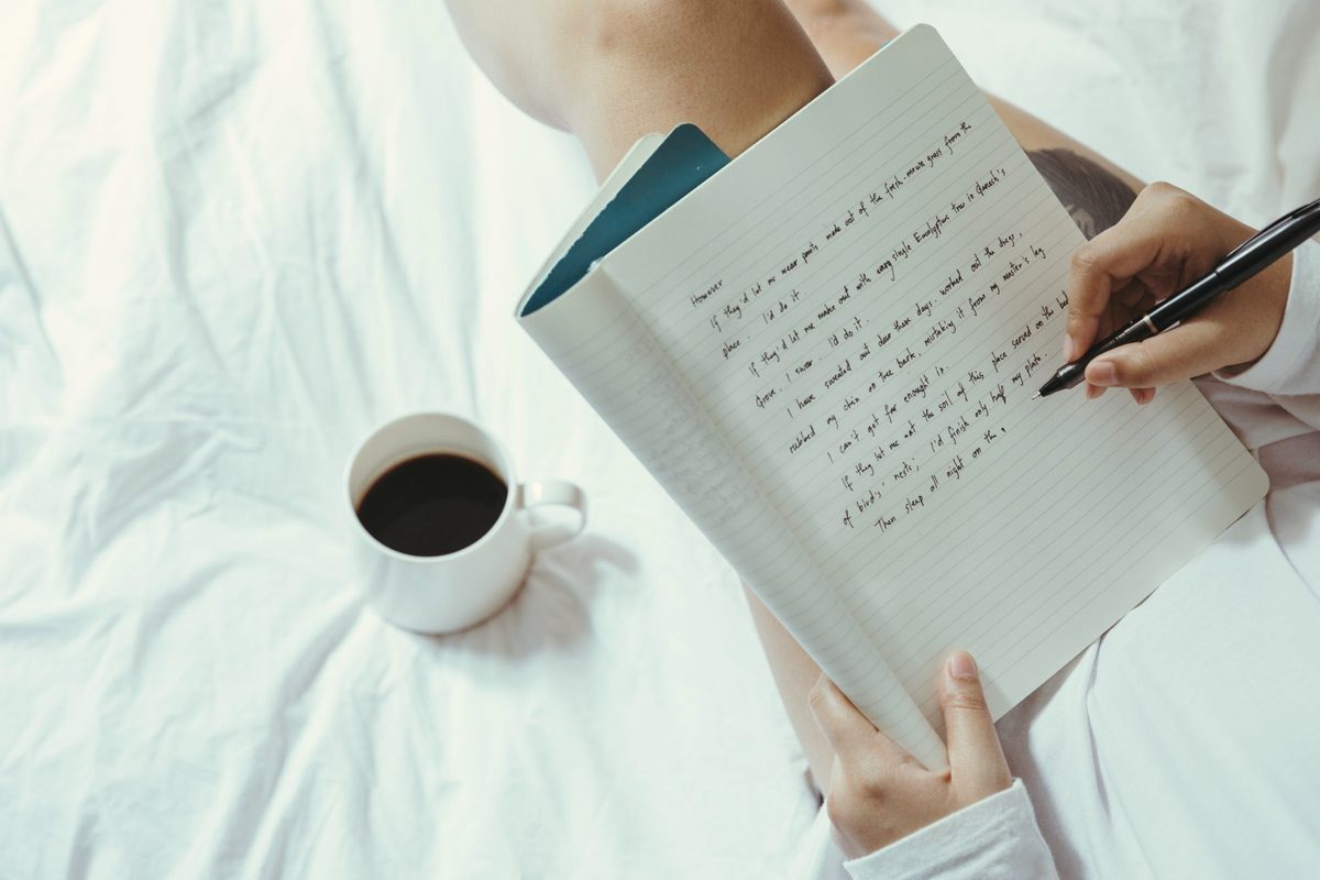 Woman writing in her journal on the bed with a coffee