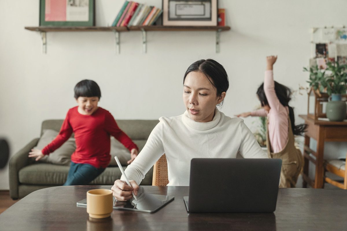 Busy mum working on laptop while children run around