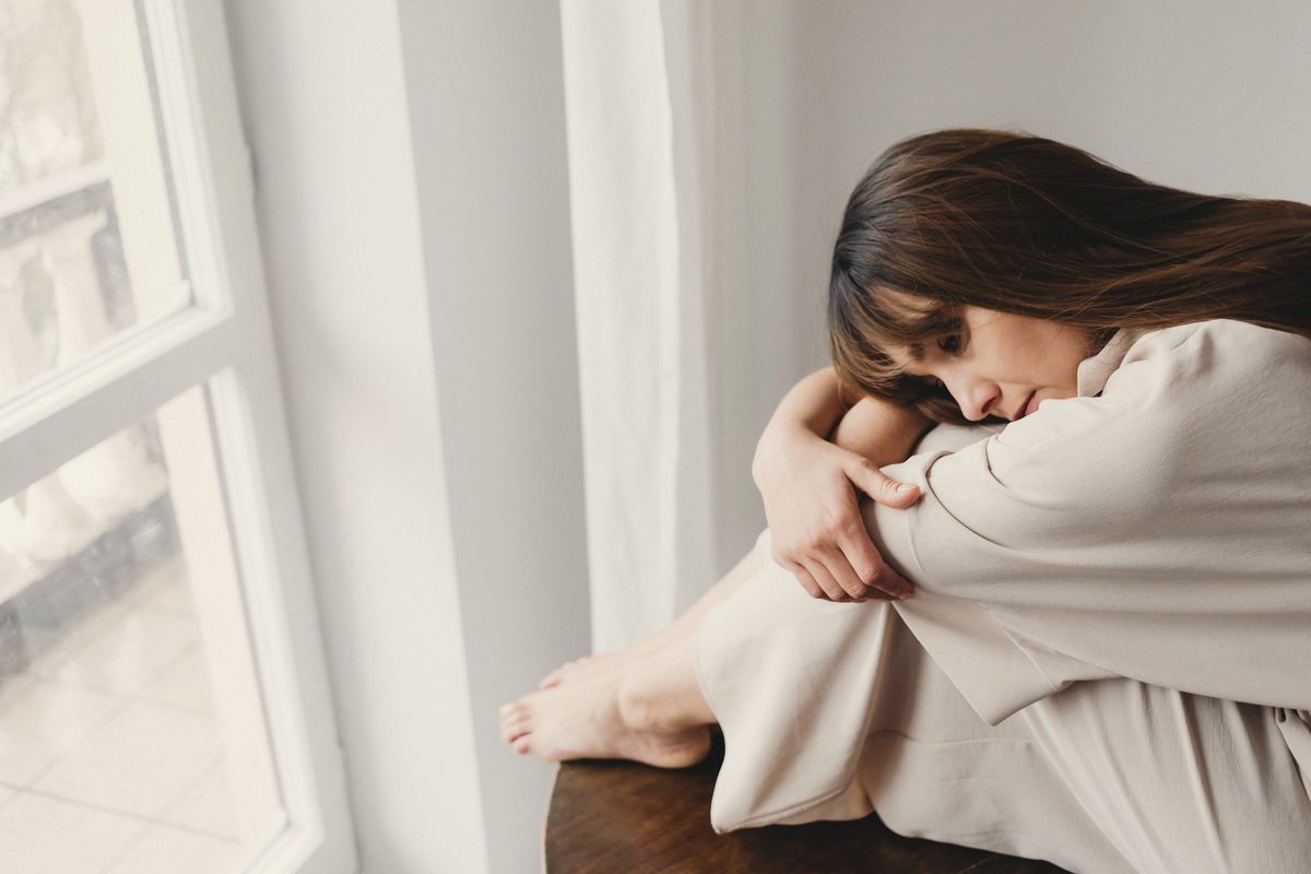 Woman sitting by the window hugging her knees