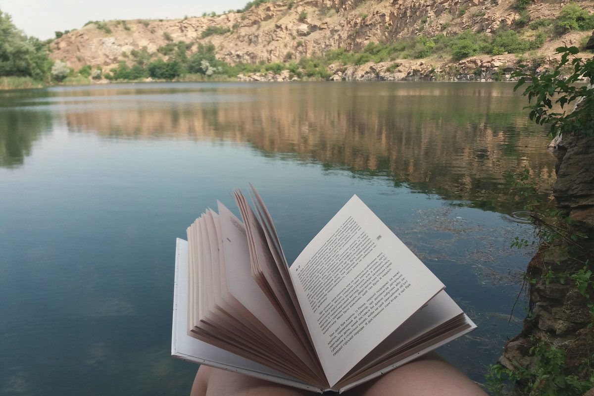 A person sitting with a book by a lake