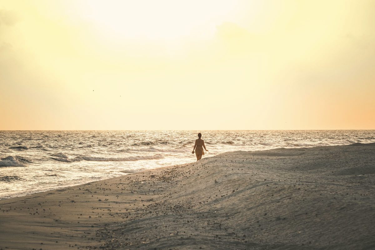Woman walking alone on the beach at sunset